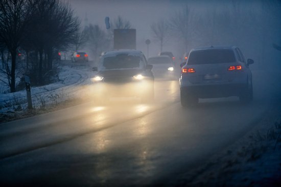 Luminous car headlights in the twilight in fog.